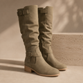 Pair of green knee-high boots with buckles on a beige background